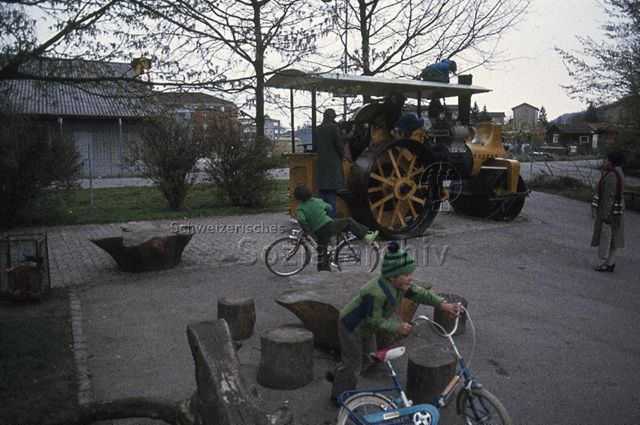 "Ausgediente Fahrzeuge, Freizeitanlage Bachwiesen" - spielende Kinder, ausrangierte Walze; um 1975