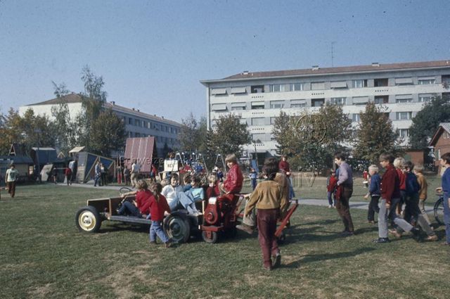 "Robinsonspielplatz Bachgraben, Basel" - Kinder fahren in einem selbstgebauten Gefährt über die Wiese; um 1975
