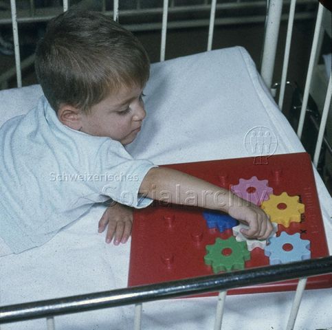 "Spielsachen für das Bettlägerige Kind" - Junge beim Spielen mit Zahnrädern; um 1975