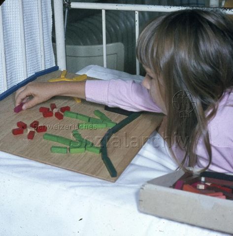 "Spielsachen für das Bettlägerige Kind" - Mädchen beim Spielen mit Holzförmchen; um 1975