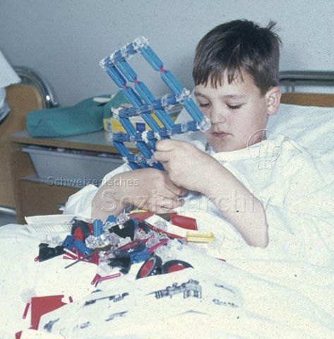 "Spielsachen für das Bettlägerige Kind" - Junge beim Spielen mit Plastikbauteilen; um 1975