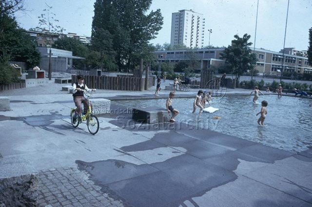 "Hirzenbach [Zürich], Planschbecken" - Kinder im Becken, ein Junge fährt auf dem Fahrrad vorbei; um 1970