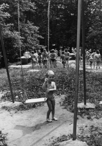 Bosco della Bella, Feriendorf für kinderreiche Familien - Junge steht neben Schaukel, im Hintergrund versammeln sich Eltern und Kinder; um 1975
