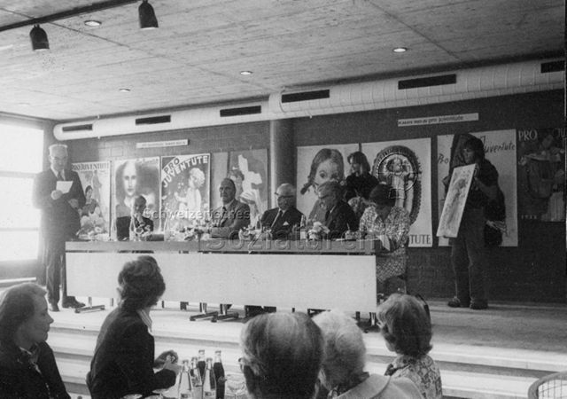 Stiftungsrat, FZA Loogarten - Willi Ritschard spricht zu den Versammelten, fünf Personen sitzen auf Podium, eine weitere Person hält ein Plakat; 08.09.1975