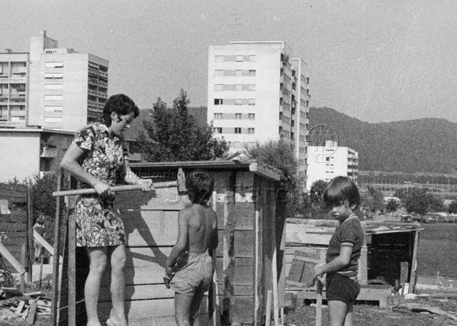 "Robinsonspielplatz Spreitenbach AG" - Mutter und Kinder beim Hüttenbauen, im Hintergrund Wohnhochhäuser; 1973