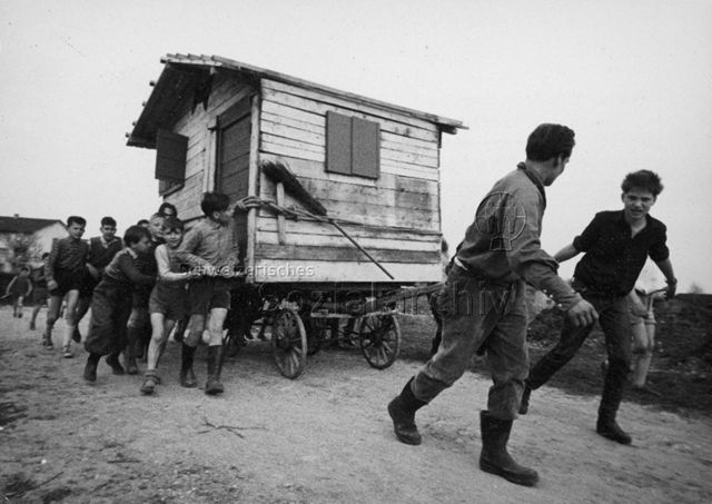 "Robinsonspielplatz Heuried" - Kinder und Erwachsene beim Transport einer Holzhütte; um 1970