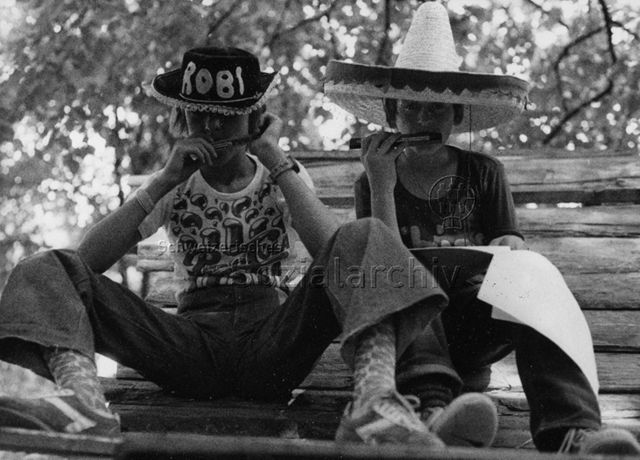 "Robi Olten" - Zwei Kinder mit Hüten beim Mundharmonika spielen; 1976