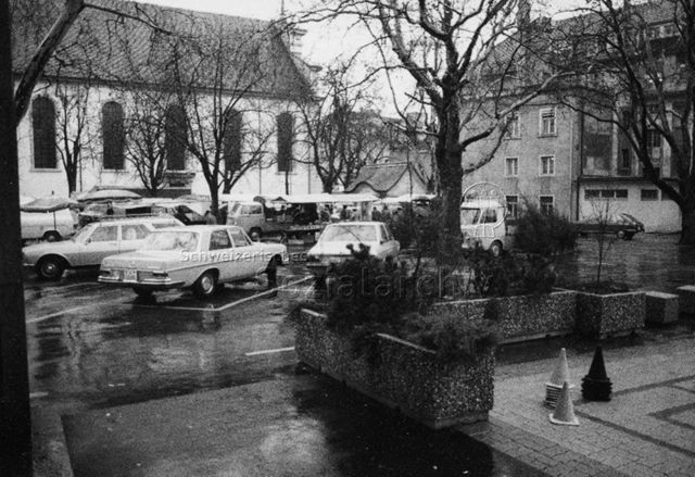 "Spielplatz - schlechte Beispiele, Olten" - Parkplatz mit Autos, Marktstände, vorne rechts ein Mühle Spielfeld; 1978