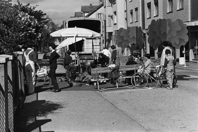 "Wohnstrassenfest, Biel" - Erwachsene und spielende Kinder hinter einem Lastwagen; um 1980