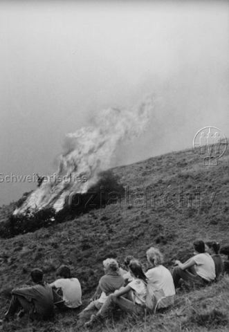 "Aktion 7, Tessin" - Verbrennen von Holzabfällen, Jugendliche betrachten das Feuer; 1988