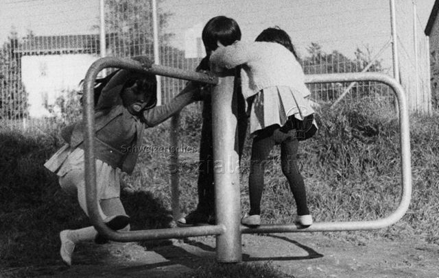 "Freizeitanlagen Schweiz", Siedlungsspielplatz Lichtensteig - Drei Kinder beim Spielen auf dem Drehkarussell; 1970