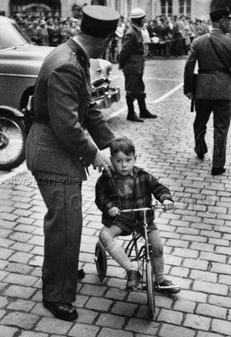 Ein Polizist steht bei einem kleinen Jungen auf dem Dreirad; um 1950