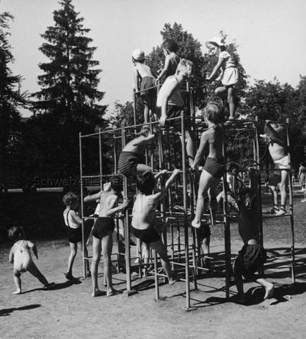 "Im Schützenmattpark in Basel sind die Spielgeräte im ganzen Park verteilt. Der Kletterturm ist auch für sehr kleine Kinder ein ungefährliches und beliebtes Gerät" - spielende Kinder am Klettergerüst; um 1960