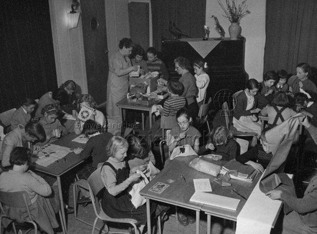"Werkarbeit in Wintermonaten in einem Vereinigungsgebäude", Niederlande (?) - Kinder und drei Lehrerinnen bei Textilarbeiten; um 1960