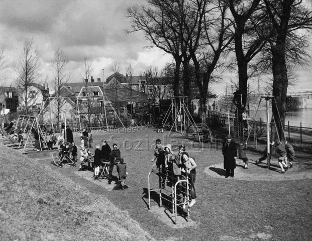 "Übersicht eines Spielplatzes in einem Dorf" in den Niederlanden (?) - spielende Kinder, Schaukel, Klettergerüst, Wippe, Karussell; um 1960