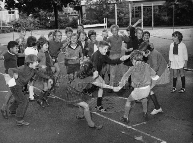 "Schule" - Vier Kinder beim tanzen oder spielen, die übrigen Kinder stehen jubelnd ringsum; um 1970