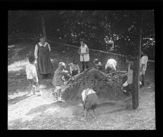 Diaserie zum Thema Kindergarten / Schulkind; Kinder mit Schaufeln und Beutreuerin um Erdhaufen stehend; um 1930