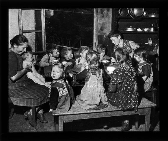Diaserie zum Alltag einer Bauernfamilie; Frau mit Kleinkind auf den Knien und weitere Kinder sitzen um Tisch; um 1930