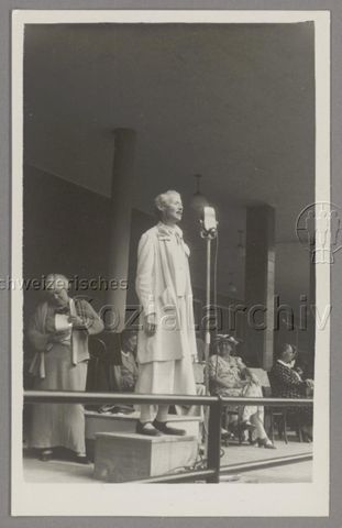 Lida Gustava Heymann auf Podest und mit Mikrophon bei Rede im Rahmen des Kongresses der Internationalen Frauenliga für Frieden und Freiheit (IFFF/WILPF) in Prag, 1929