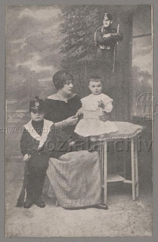 Frau mit Kleinkind und Knaben in Füsilieruniform und mit Gewehr, oben rechts: hineinretuschierter Mann in Füsilieruniform der Schweizer Armee (?), Postkarte datiert: 1915